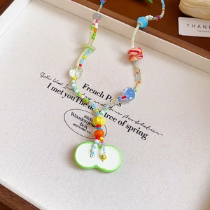 Close-up of colorful beaded necklace with a green apple charm in a white jewelry tray