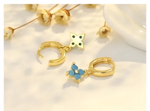 Nahaufnahme von goldenen Creolen mit blauen Kleeblattanhängern und Zirkonia