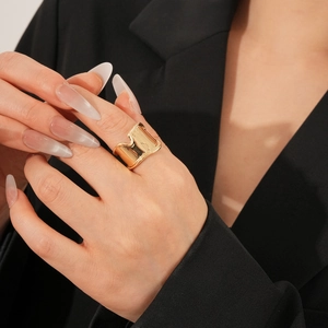 Detail of wide gold textured ring with geometric wavy grooves worn on index finger