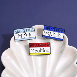Three creative enamel pins with name tag designs on a white shell-shaped ceramic plate