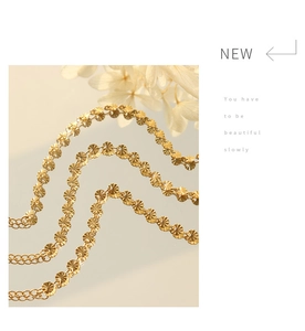 Detail of a gold metal chain bracelet with sunburst texture charms and white flowers