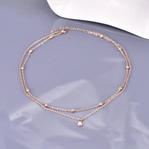 Detail of rose gold double-layer necklace featuring small metal beads and a zircon pendant