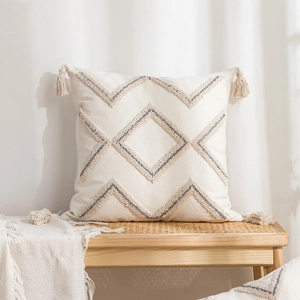 Square cream tufted throw pillow with blue geometric diamond patterns and tassels