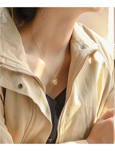 Close-up of a gold vintage star coin pendant necklace worn by a fashion model on a beige jacket