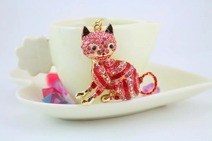 Detail of a golden cat pendant with pink rhinestones on a white heart-shaped tray