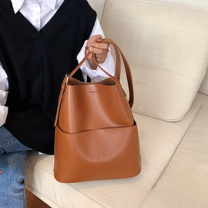 Detailansicht der großen braunen Leder-Eimertasche auf einem cremefarbenen Sofa
