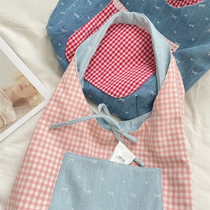 Detail of denim and plaid patchwork apron featuring bow embroidery and front pocket