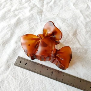 Detail view of a 10cm amber tortoiseshell bow hair claw clip measured with a ruler