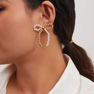 Detail of elegant bow stud earring with white pearl and gold bead on model's ear