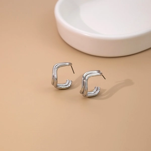 Macro detail of silver geometric C-shape earrings on white ceramic tray