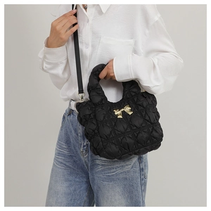 Detail of black quilted nylon bag with golden bow and detachable shoulder strap