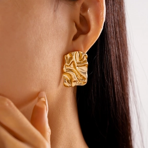 Close-up of a model wearing a gold crumpled metallic square stud earring with wavy texture