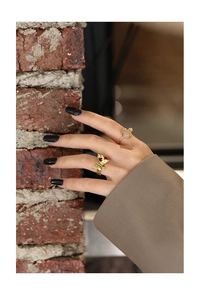 Detail of golden butterfly wide ring and gemstone band worn against a rustic brick wall
