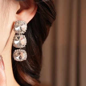 Close-up of silver earrings with three round crystals and micro-pavé diamonds on a model