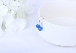 Detailed view of translucent blue agate bead earrings with silver hooks on white porcelain