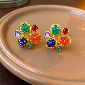Detailed view of vintage gold woven earrings with multi-colored gemstones on a ceramic plate