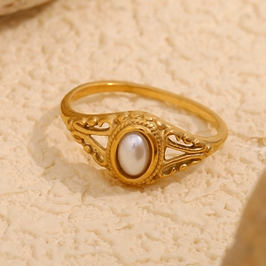 Detailed view of an ornate gold flower ring set with a white oval pearl on a textured surface