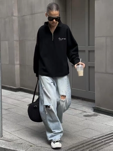 Street style view of a black quarter-zip sweatshirt with white script chest printing
