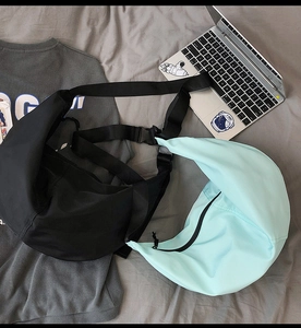 Flat lay of nylon crescent crossbody bags in black and mint green on a grey bed