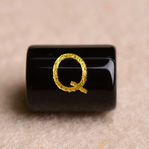 Macro view of a polished black onyx bead featuring a textured golden letter Q engraving