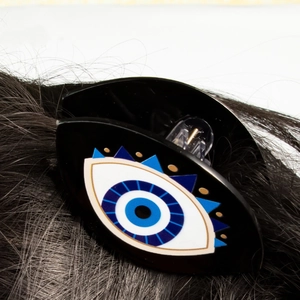 Macro shot of a black hair claw clip with blue evil eye patterns on dark hair