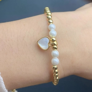Detail of beaded bracelet with gold beads, pearls and heart shell pendant on wrist