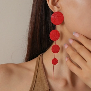 Detail showing long red tassel earrings with textured circular disks on a model