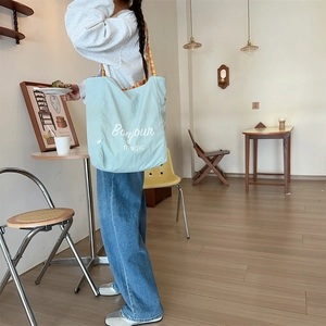Light blue canvas tote bag with 'Bonjour' text shown in a cozy cafe setting
