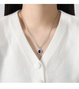 Detailed close-up of a blue sapphire halo necklace on a model wearing white knitwear