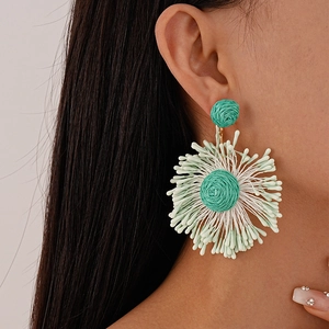 Close-up of mint green handmade woven flower tassel earrings on model during wear