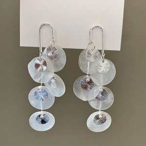 Detail view of long shell tassel earrings with white layers and silver metal discs