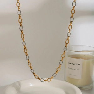 Detailed view of two-tone 18k gold and silver stainless steel chain necklace on ceramic