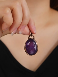 Close-up of purple amethyst raw stone pendant in bronze frame held by hand