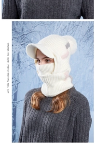 Detail of white knit balaclava with pompom and peak visor on model in snow