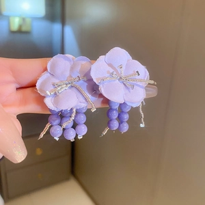 Dettaglio di orecchini a petalo di stoffa viola con stami di strass e nappe di perline