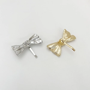 Detail of silver and gold metal bow hair clips with textured pleated surface finish