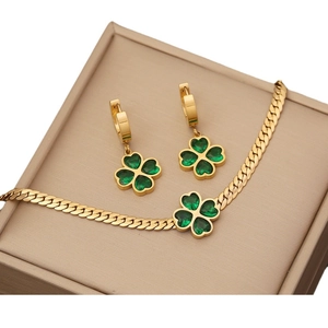 Golden clover jewelry set with emerald stones on a beige jewelry box surface
