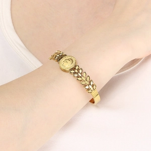 Detail of a gold-plated olive branch bracelet with a relief coin pendant on wrist