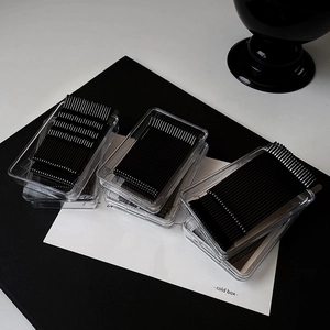 Minimalist black metal hair clips organized in transparent rectangular boxes on a sleek background