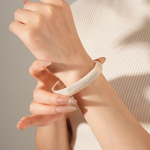Close-up of minimalist cream resin bangle worn with a textured beige knitted sweater