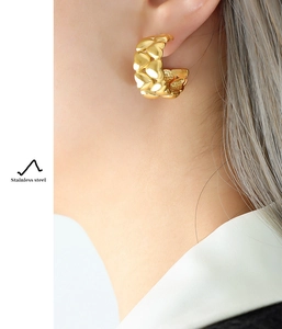 Detail of gold-plated stainless steel heart earrings worn on ear showing embossed texture