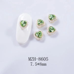 Détail macro d'un bijou d'ongle cœur 3D avec pierre verte et mini perles sur un ongle blanc