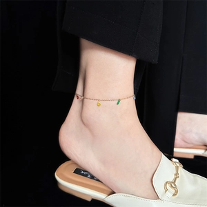 Close-up of golden anklet with teardrop colored gemstones on a woman's ankle