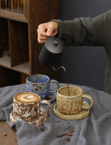 Close-up of coffee pouring into handmade ceramic mugs with speckled glaze and latte art