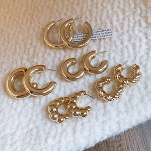 Flat lay of five pairs of golden C-shaped hoop earrings on white fabric texture