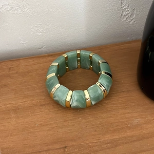 Détail du bracelet en résine marbrée vert et blanc avec séparateurs dorés sur bois