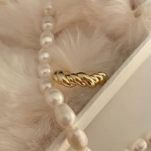 Close-up of golden twisted knot ring on creamy faux fur with elegant pearl accents
