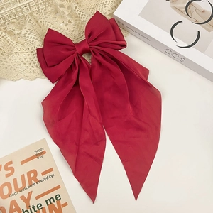 Detail of a large dark red silk bow hair clip with long ribbons on lace background