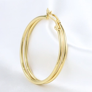 Macro detail of 50mm gold stainless steel hoop earrings on elegant white satin background