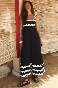 Detail view of a long black dress featuring white scalloped trim in an outdoor setting